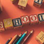 From above of wooden cubes making word school placed near color pencils on red table
